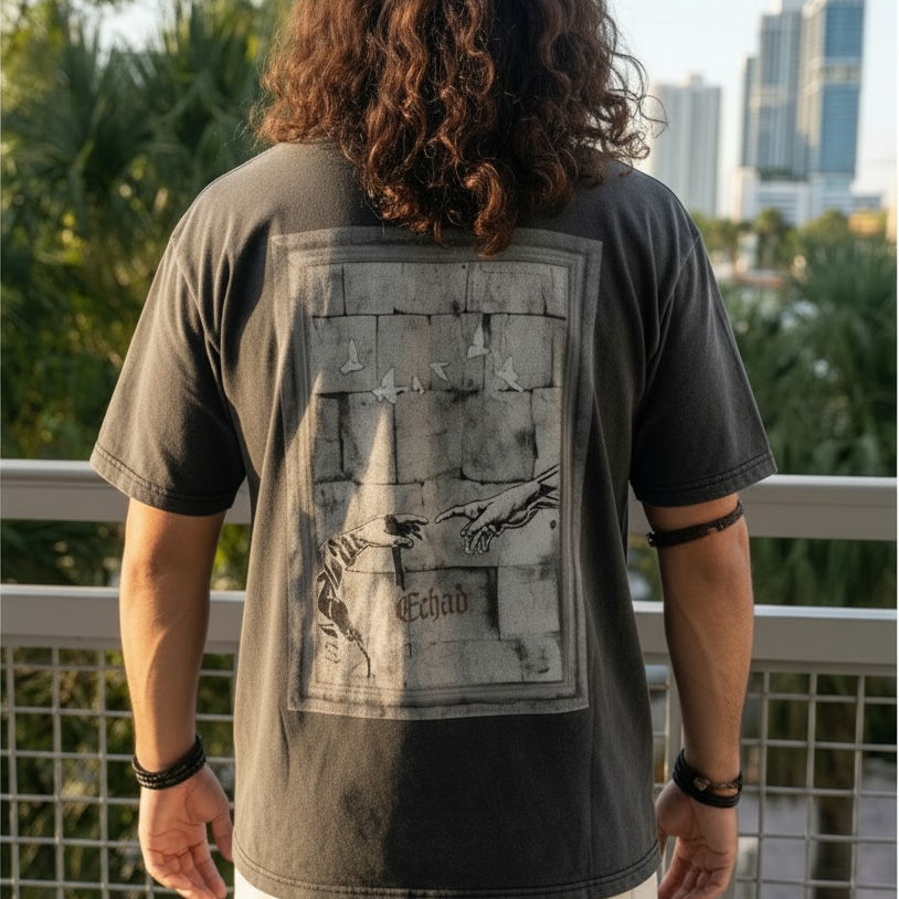 Person wearing a dark t-shirt with a graphic design on the back, standing on a balcony with a cityscape view.