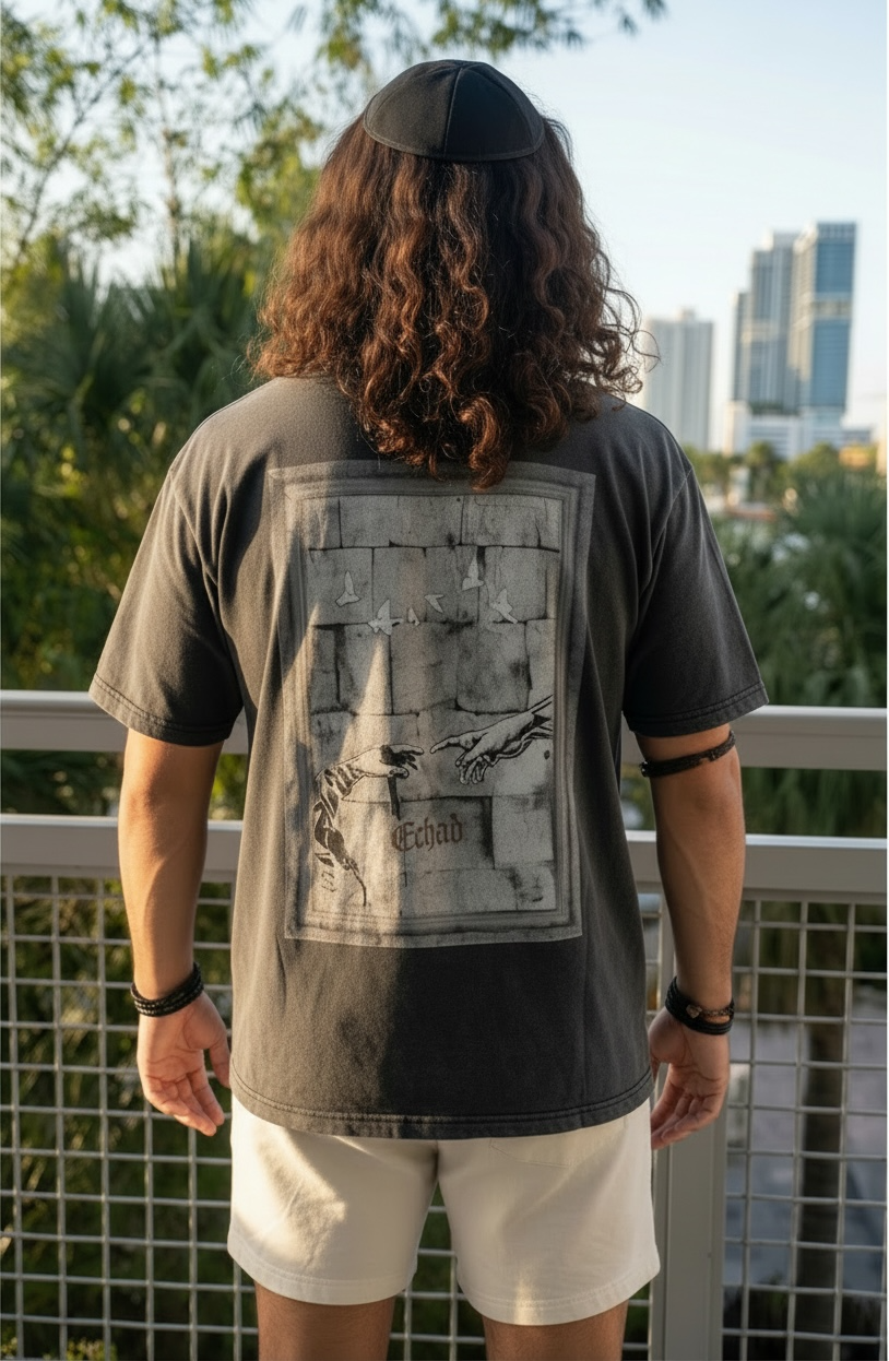 Person wearing a dark t-shirt with a graphic design on the back, standing on a balcony with a cityscape view.
